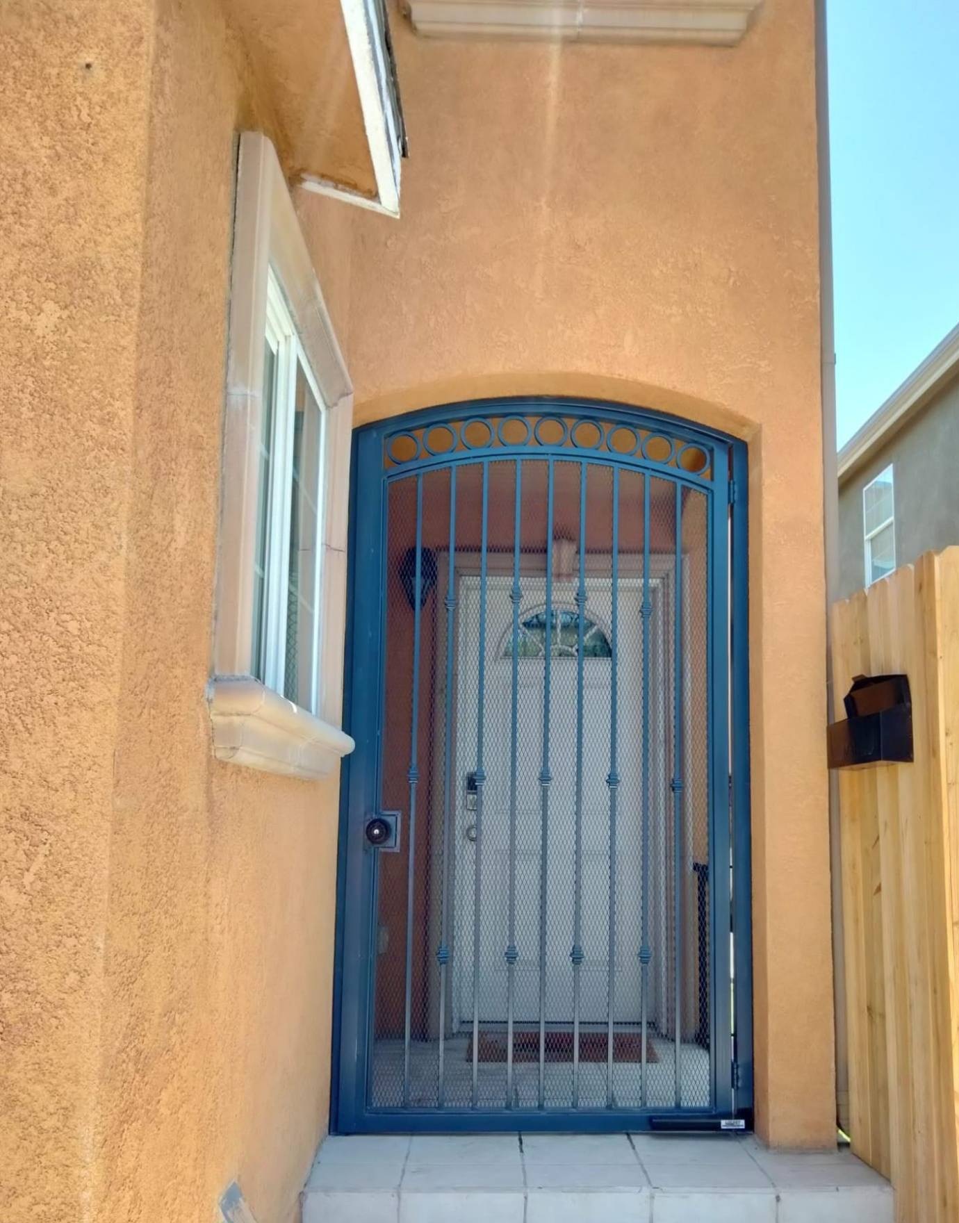 Arched dark blue pedestrian entry gate with ring detail and mesh backing at a front door