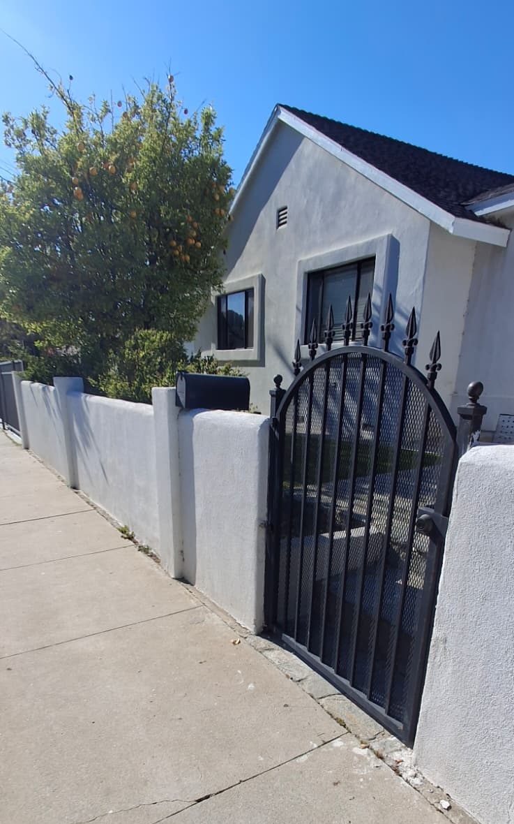 Arched black pedestrian gate with spear finials set in a white stucco wall