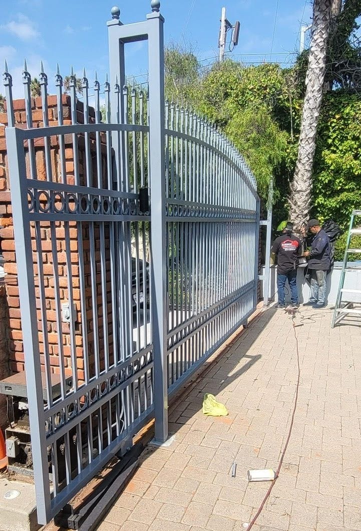 Gray arched wrought iron sliding gate on its track with operator, during installation