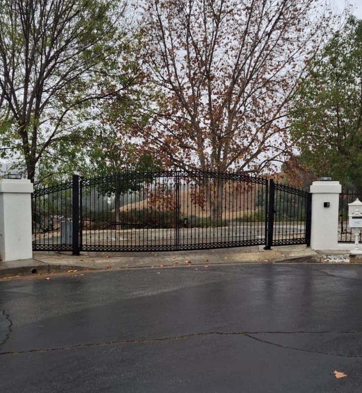 Black wrought iron double swing driveway gate with arched top between white pillars