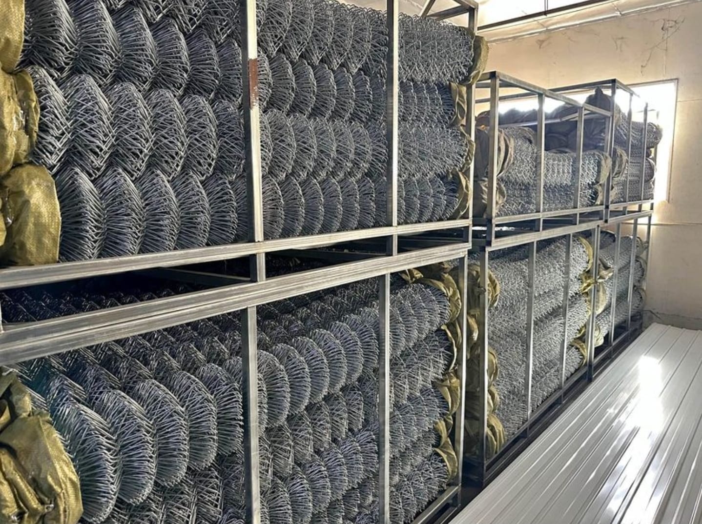 Rolls of galvanized chain link fence fabric stacked on metal racks