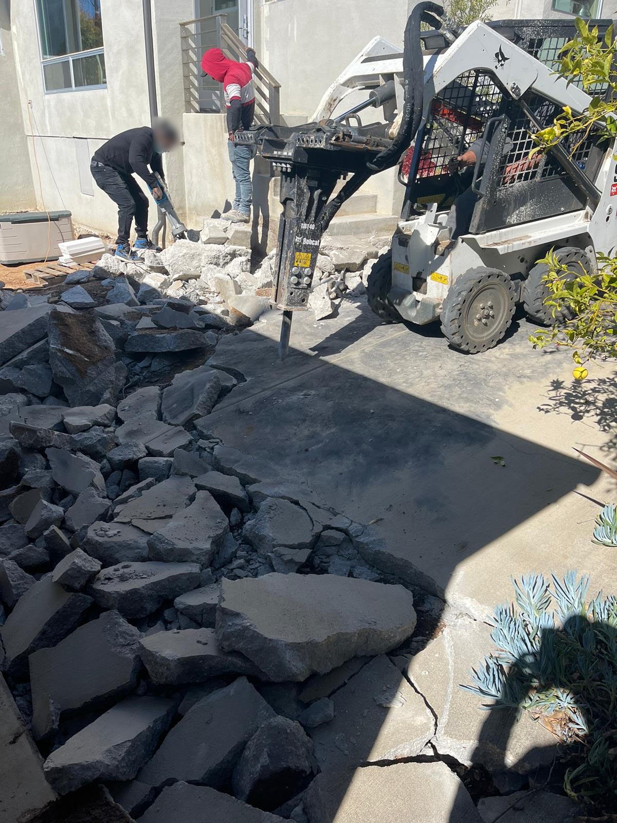 Crew removing an old concrete driveway with a skid-steer breaker before new paving