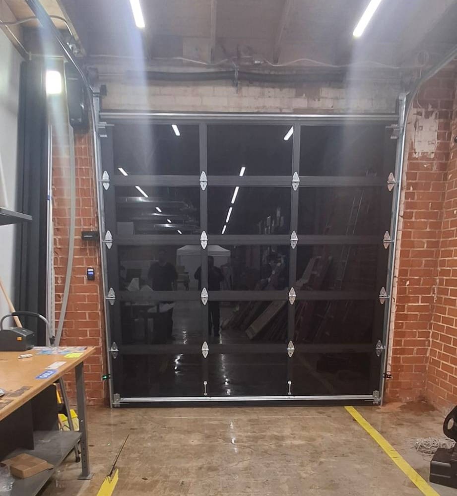 Glass sectional garage door on overhead tracks inside a warehouse, with an access reader beside it