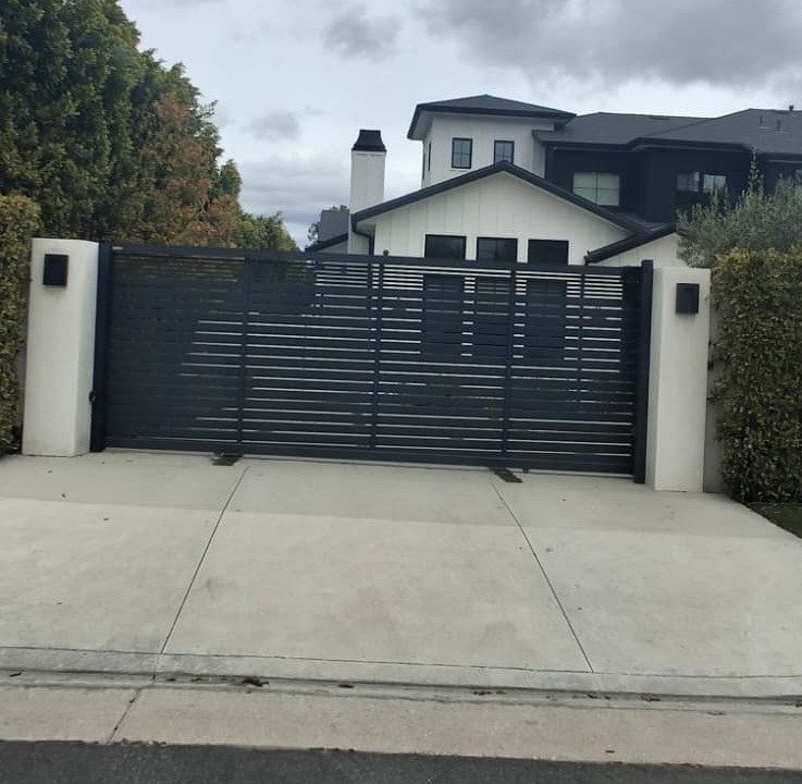 Dark horizontal slat wrought iron sliding gate between white stucco pillars