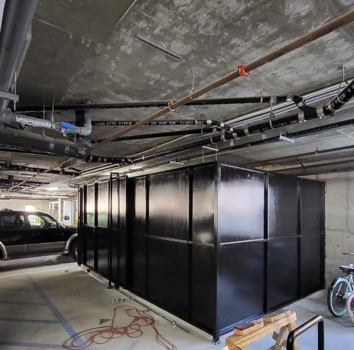 Side view of a black solid metal-panel storage enclosure inside a parking garage