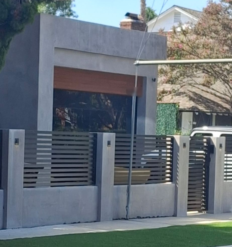 Modern gray block wall and pillars with pillar lights, slat fence panels, and a pedestrian gate