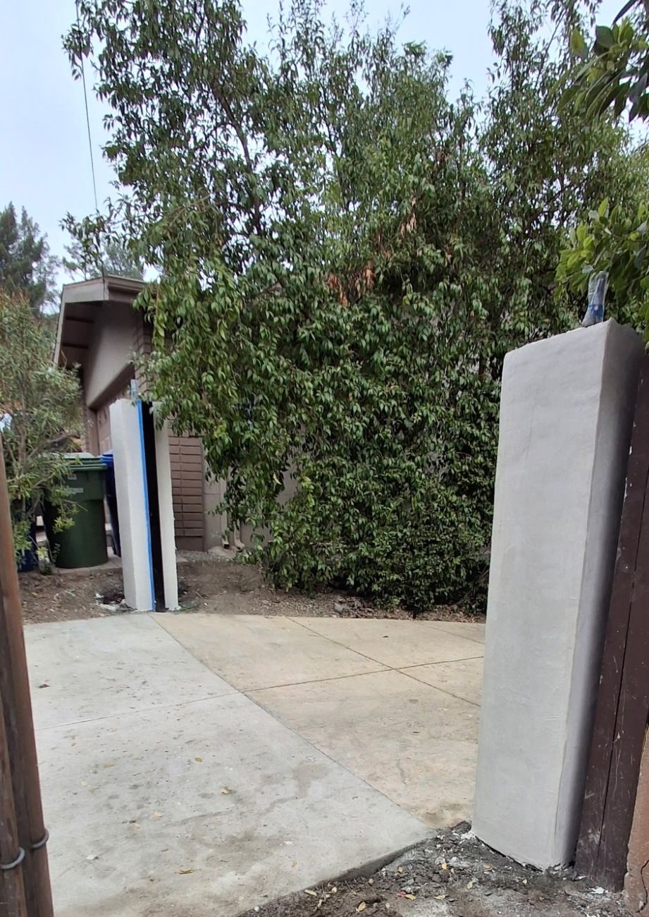 Newly built stucco-finished driveway gate pillars on either side of a concrete driveway