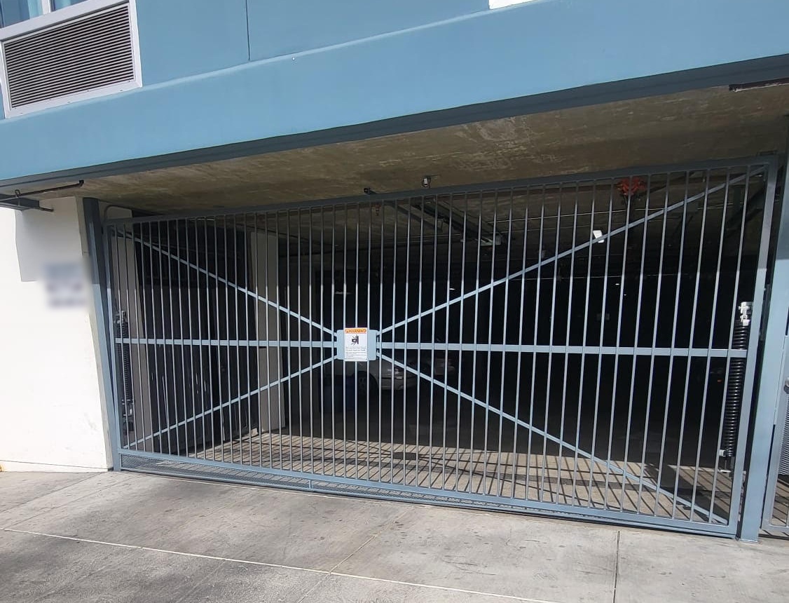 Gray overhead driveway gate with vertical pickets and X-brace design at a parking garage entrance