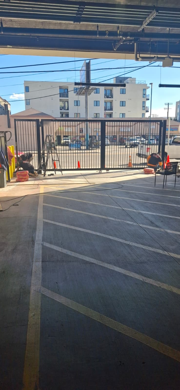 Crew finishing wrought iron swing gates at a parking garage entrance, viewed from inside