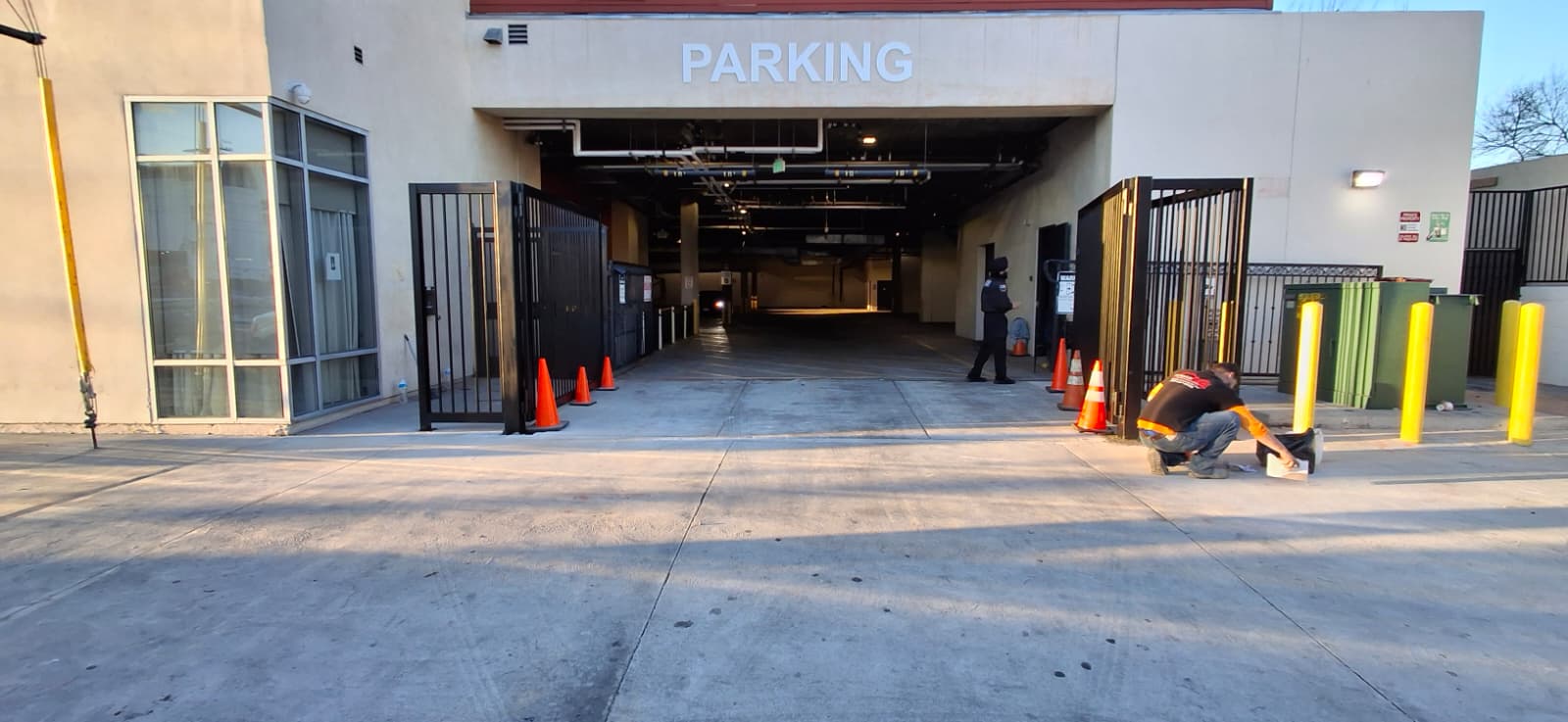 Black wrought iron swing gates open at a parking garage entrance during installation