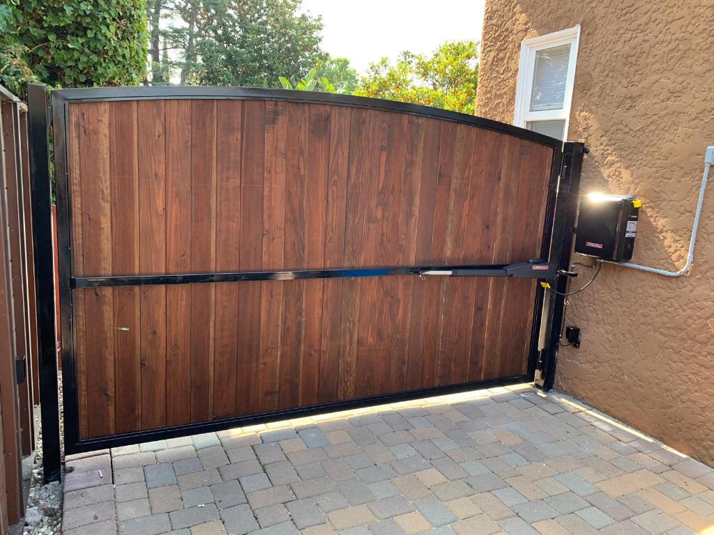 Paver driveway leading to an arched wood and steel driveway swing gate with automatic operator