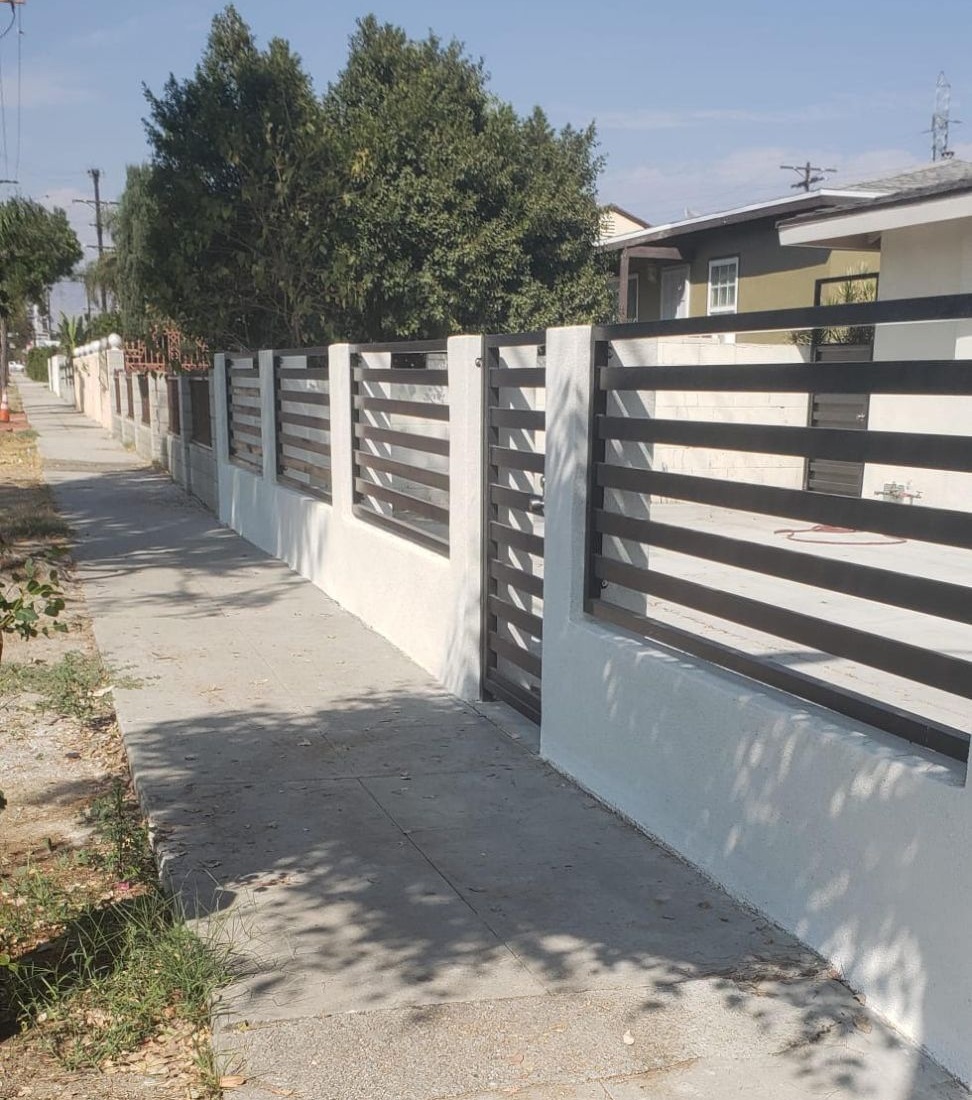 Dark horizontal slat fence on a white stucco block wall with matching pedestrian gate along a sidewalk