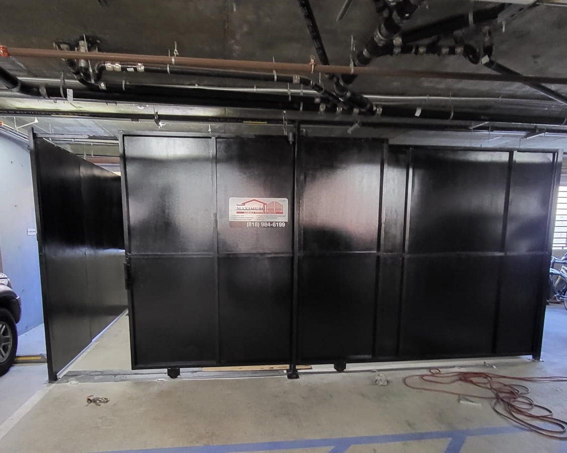 Black solid metal-panel storage enclosure with sliding doors in a parking garage