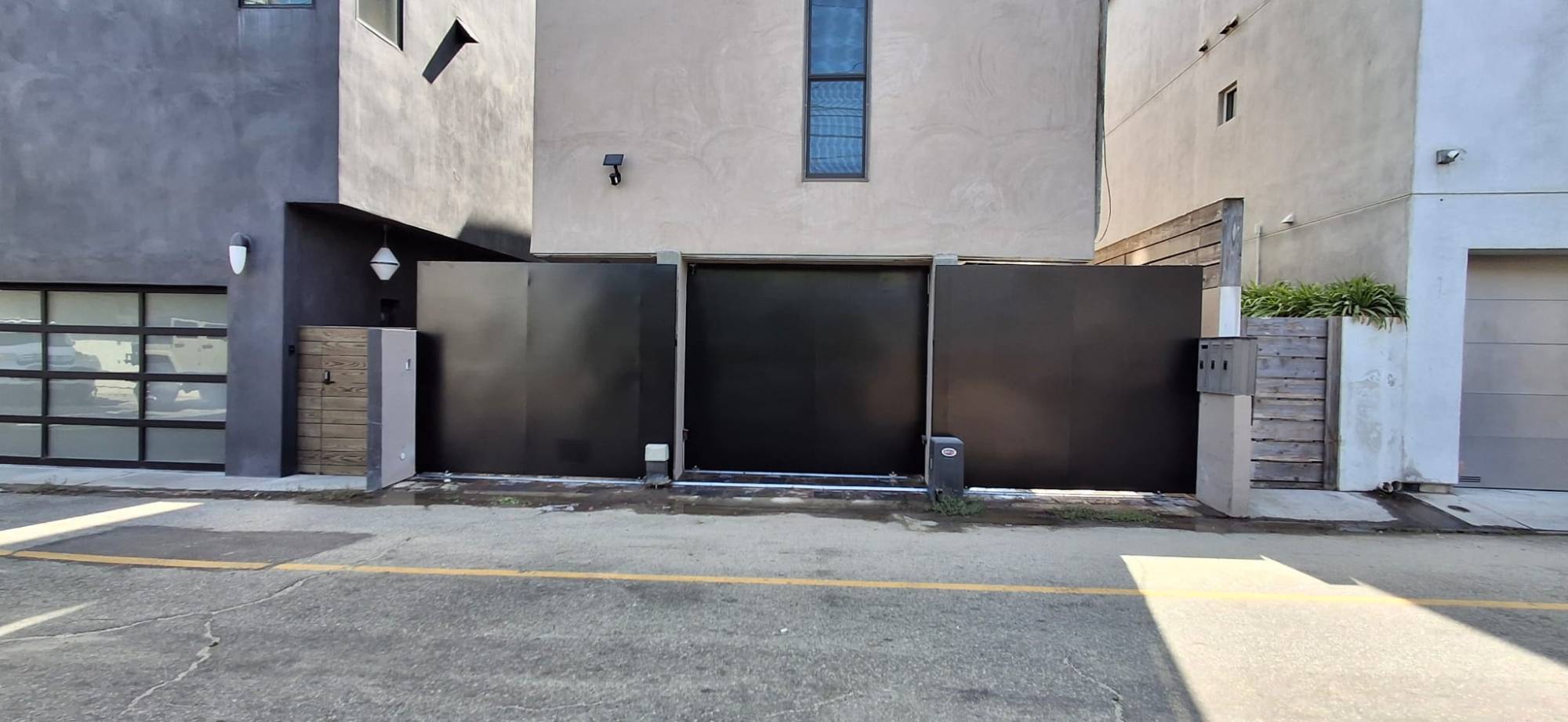 Solid black wrought iron sliding gate panels across an alley driveway with gate operator