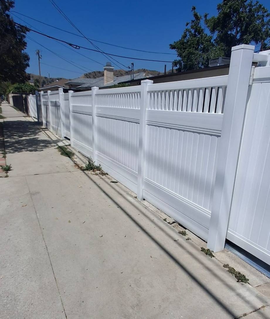 White metal privacy fence with decorative picket-style topper along a residential sidewalk