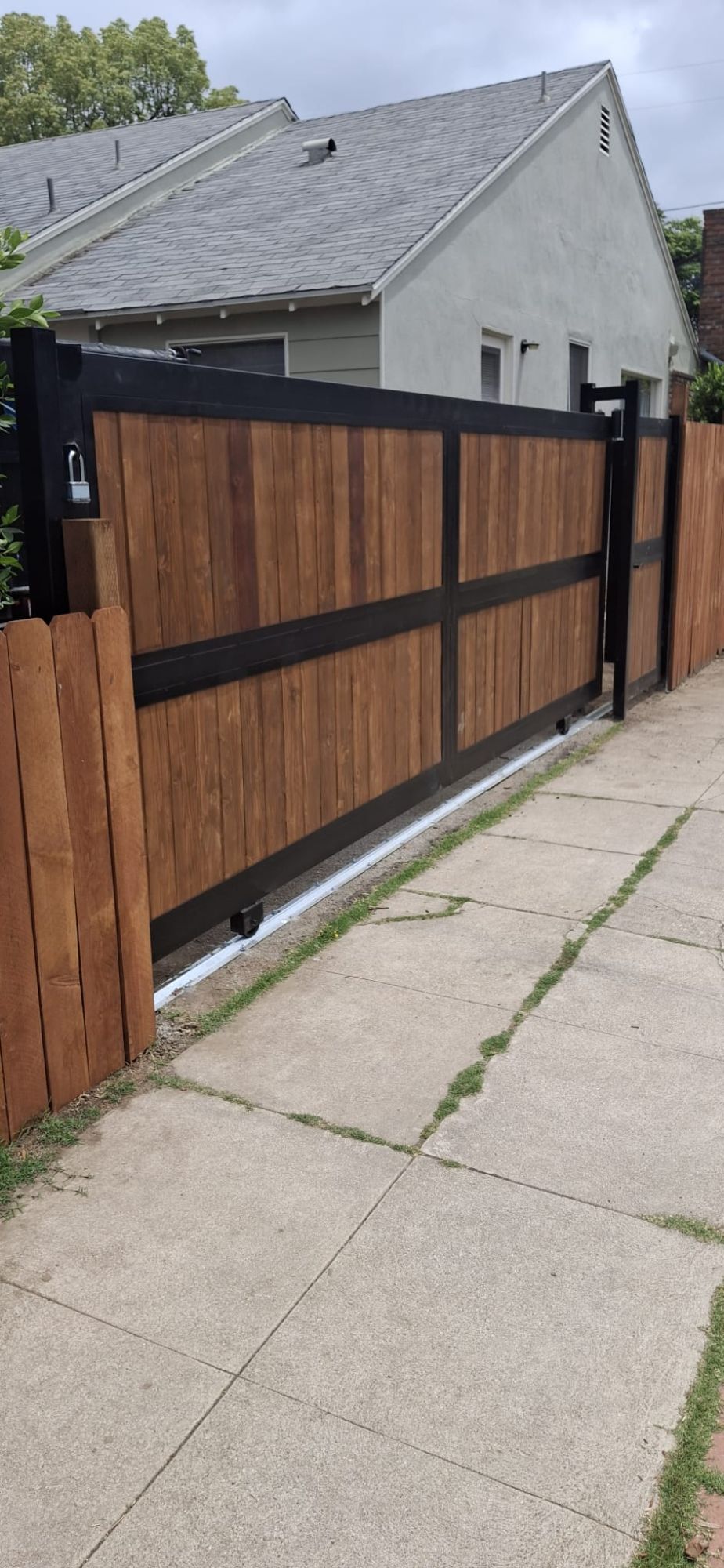 Sliding driveway gate with stained wood boards in a black wrought iron frame