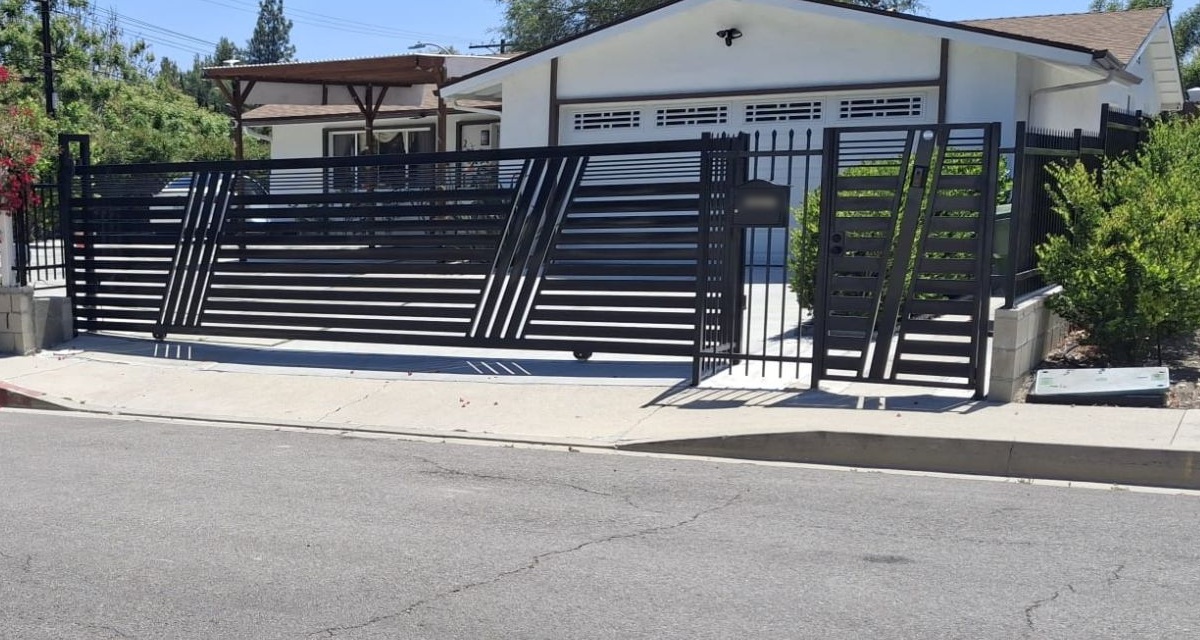 Black wrought iron sliding gate with horizontal slats, diagonal accents and matching pedestrian gate